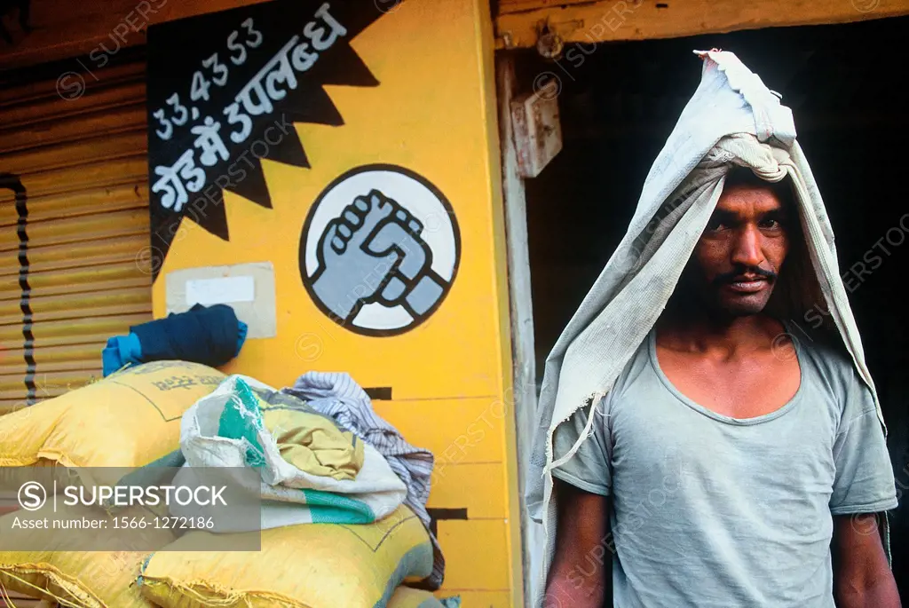 Worker whose work is to load and download sacks of cement near the logo of the company for which he is working. India.