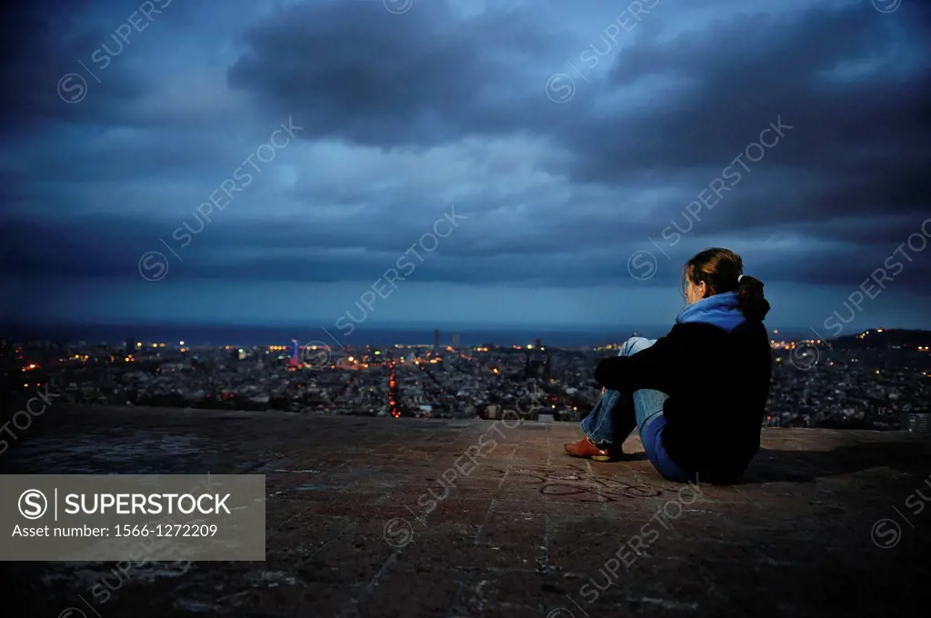 A woman observes the illuminated Barcelona Skyline by night, Spain.