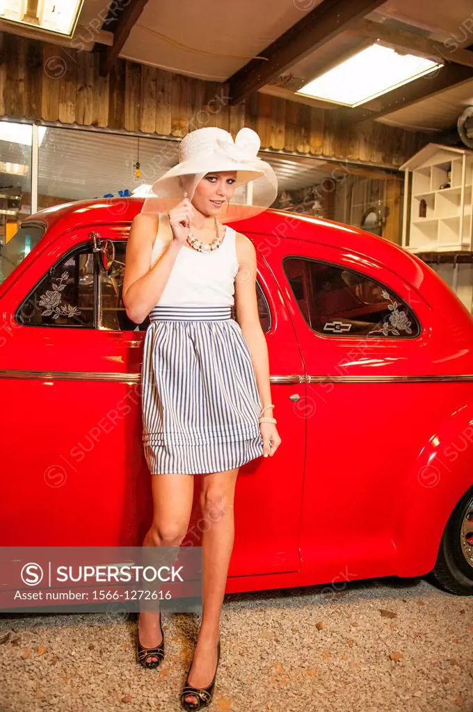 Female model in wide-brimmed white hat by antique red automobile