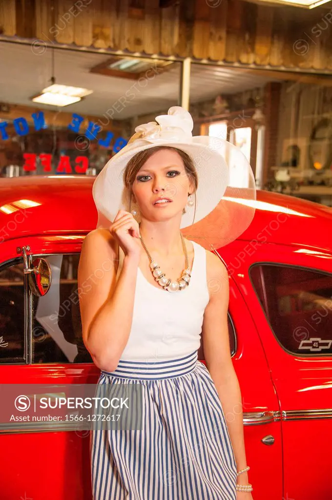 Female model in wide-brimmed white hat by antique red automobile