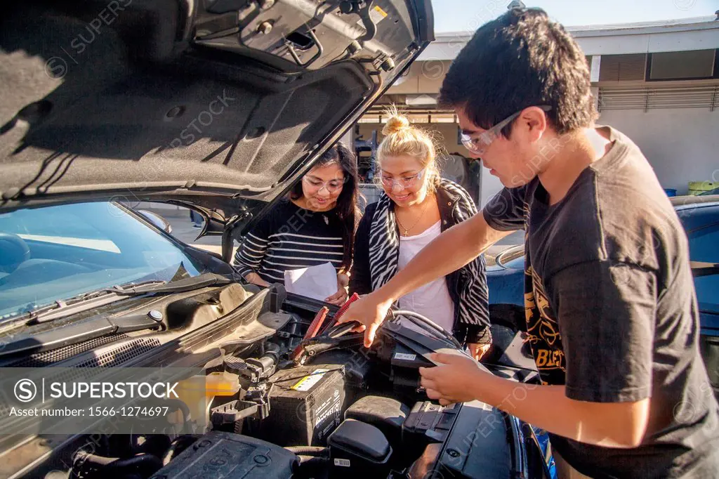 Wearing safety glasses Hispanic and Caucasian teenage girls learn how to charge a battery in auto shop class in San Clemente, CA.