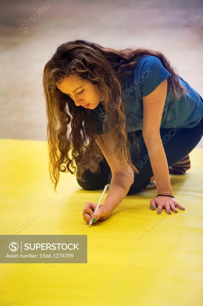 Kneeling on a sheet of yellow poster paper, a high school girl outlines lettering for a school play advertisement in San Clemente, CA.
