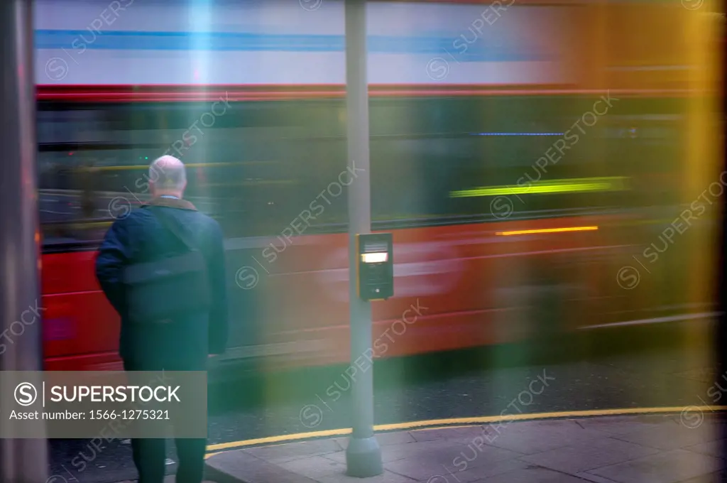 Person above a sidewalk waiting to cross while passing a bus on a street in London