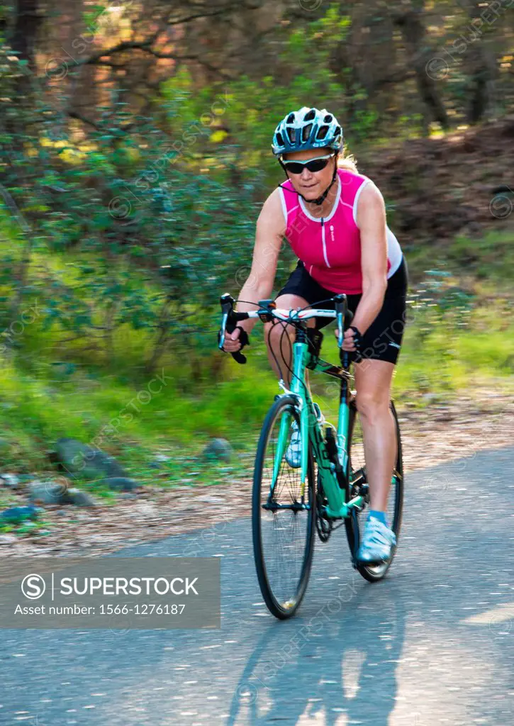 A middle aged woman cycles along a wooded trail.