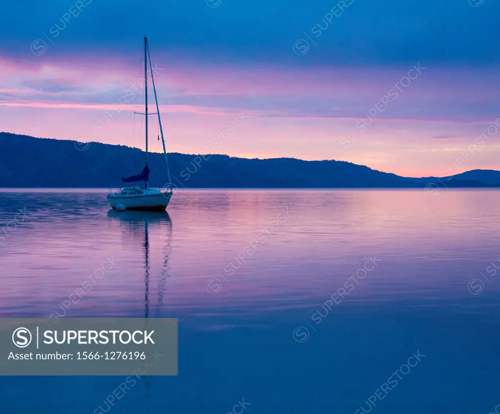 A sailboat is reflected in the dawn glow on California's Clear Lake.