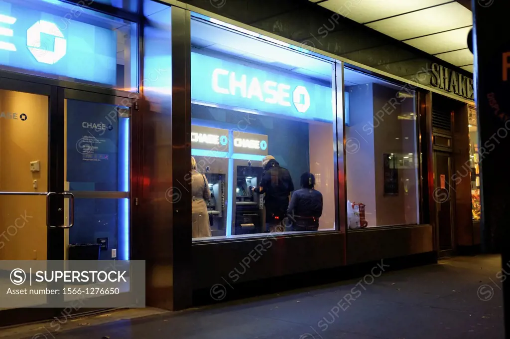 Three People at a Bank Vestibule ATM Machine at Twilight.