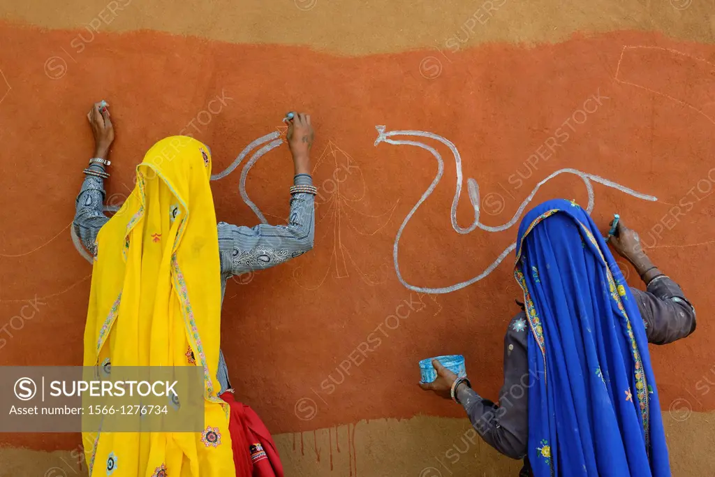 India, Rajasthan, Tonk region, Women painting clay walls prior to Diwali festival.
