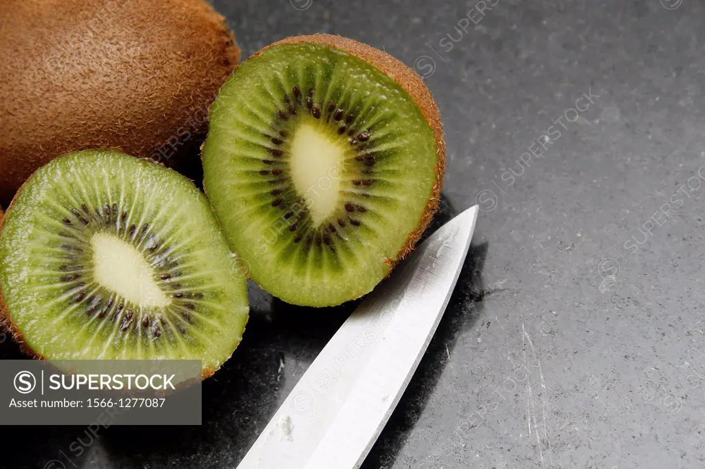 cut open kiwi with stainless steel knife on marble chopping board.