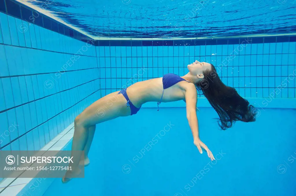 Young woman wearing a bikini while swimming under water in a open-air pool.