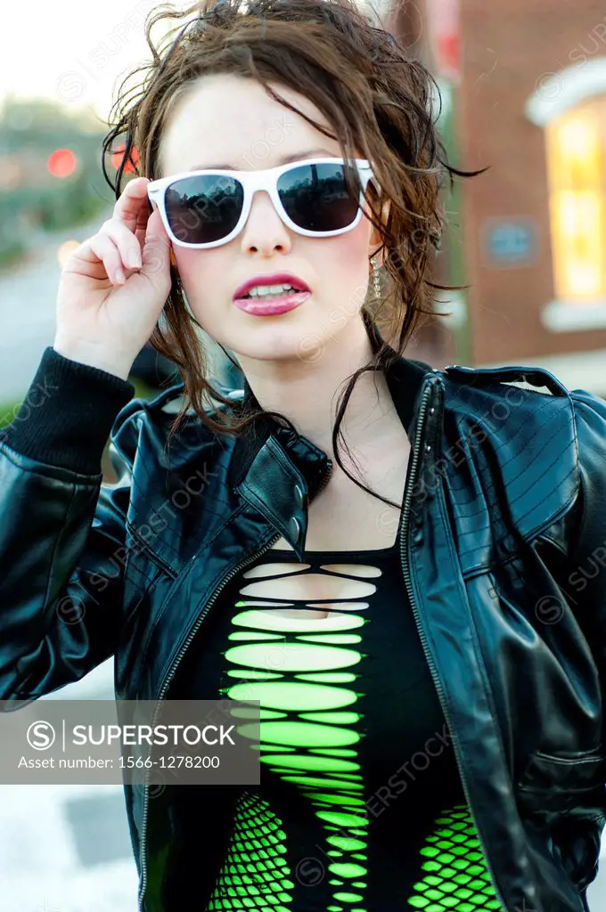 A 24 year old brunette woman in weaing blue leggings and a black jacket walking across a street.