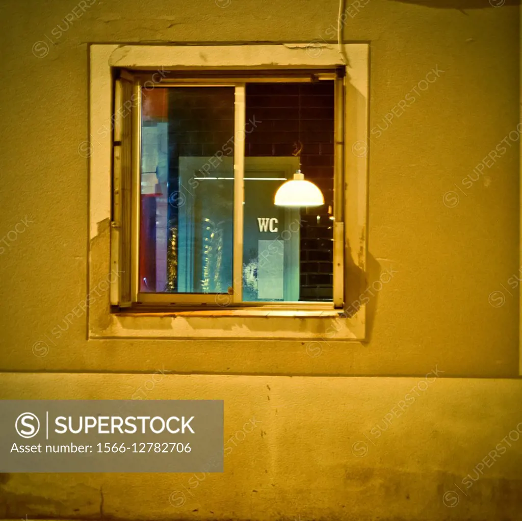 Window in street at night. Interior room  view with lighted lamp and WC sign. Barcelona, Catalonia, Spain.