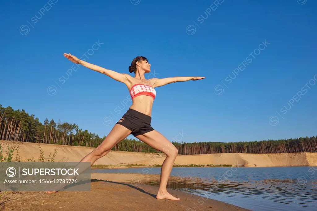 Young woman doing yoga on a beach next to a little lake.