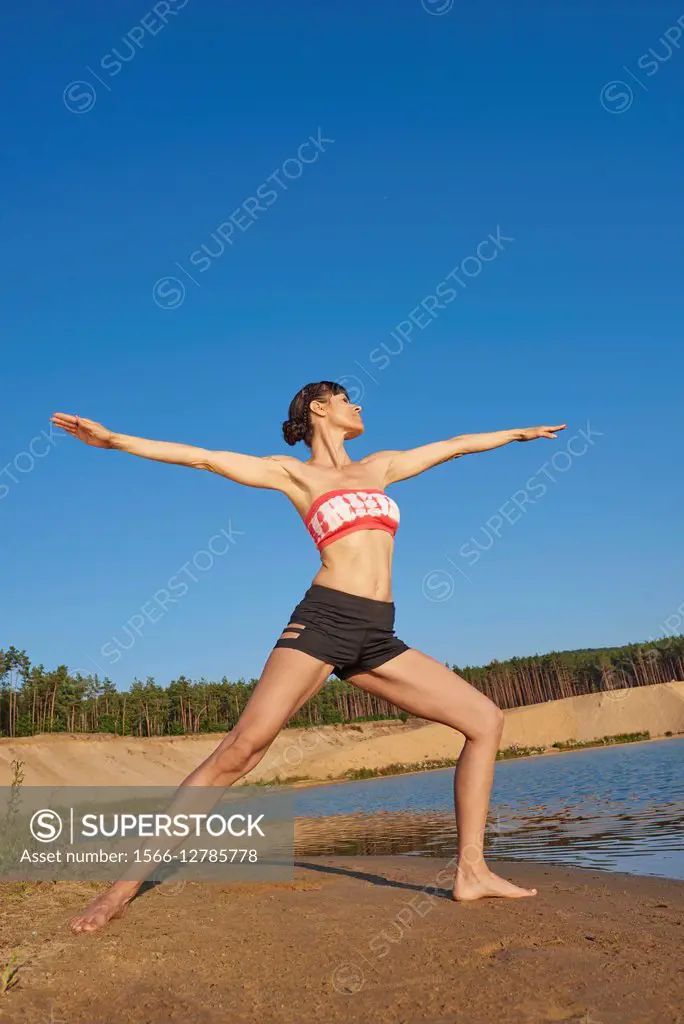Young woman doing yoga on a beach next to a little lake.
