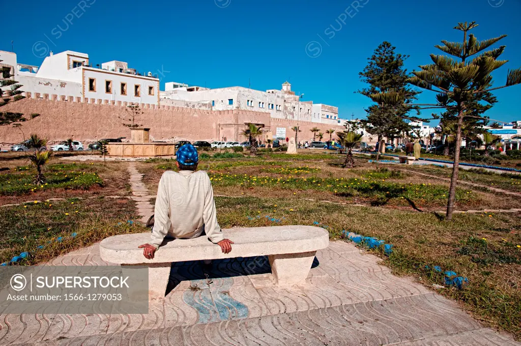 Man sitting on a bench of a park in front of Essaouira medina wall, Essaouira, Morocco.