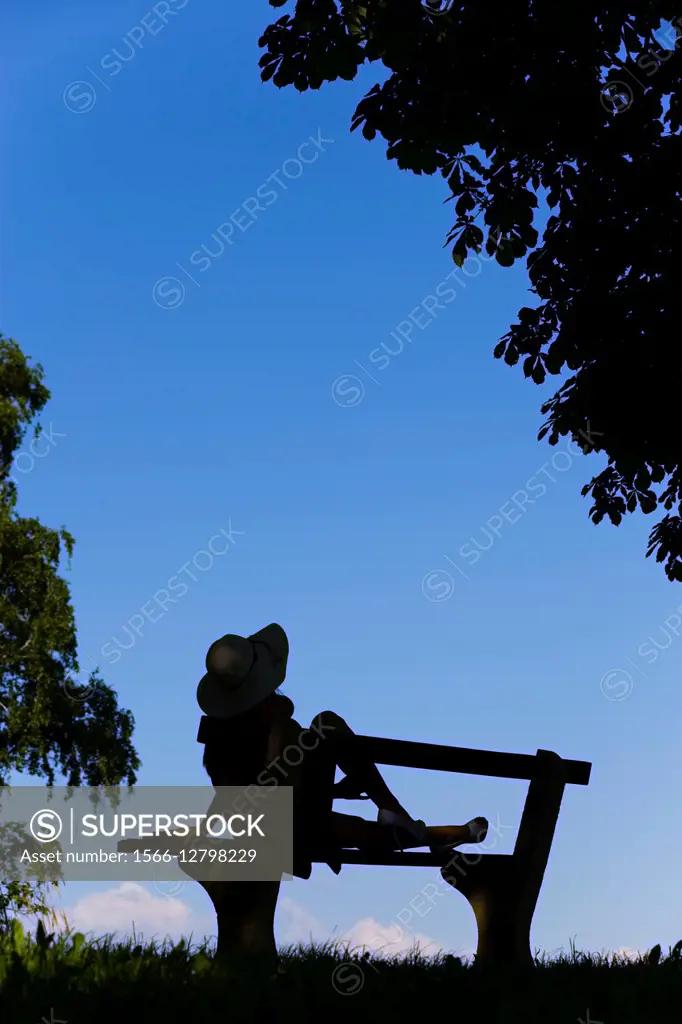 Young female on bench silhouetting against Blue sky