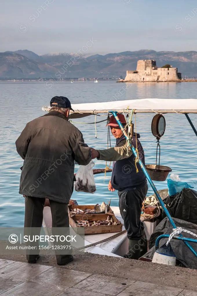 Selling fish from a fishing boat in the harbour at Nafplio with the Bourtzi island and fort in the background, Argolid, Peloponnese, Greece.
