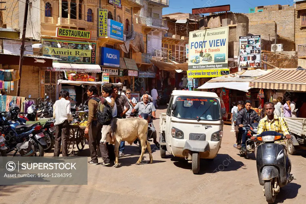 Jaisalmer street scene with cow, tuk tuk and motorbike, Jaisalmer, Rajasthan State, India.