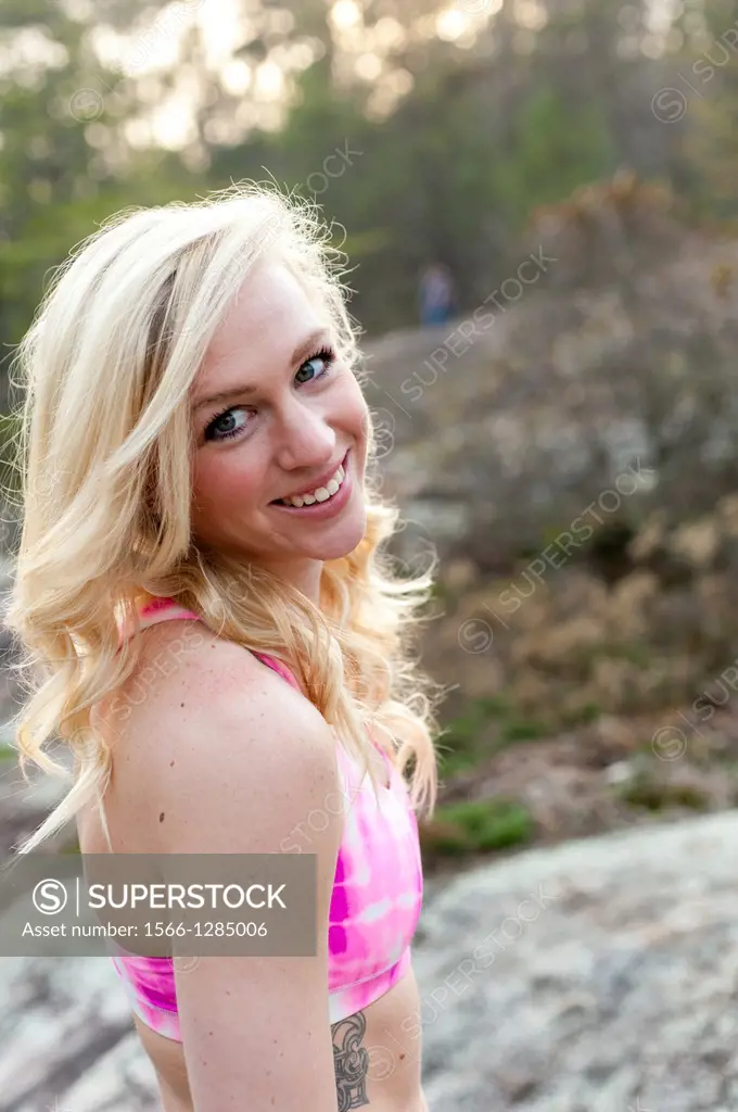 A 23 year old blond woman wearing a pink sports bra outside smiling at the camera.