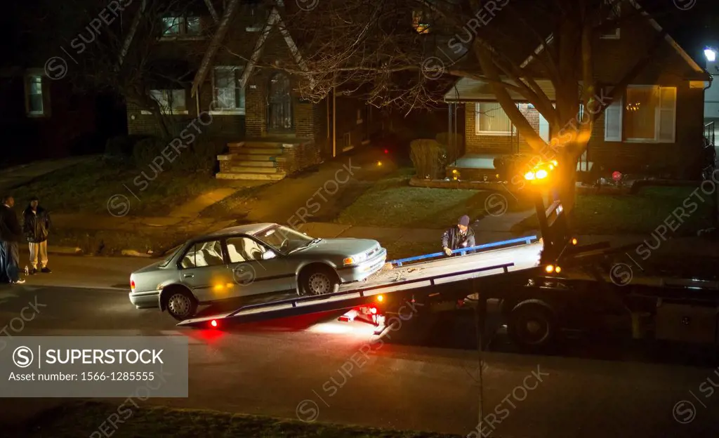 Detroit, Michigan - A worker loads a disabled car onto a truck at night in a residential neighborhood.