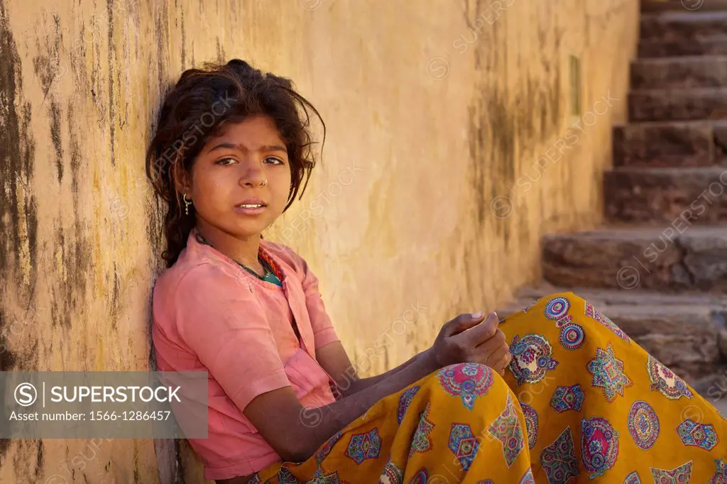Portrait of poor young indian girl siting on the stairway to Amber Fort, Jaipur, India.