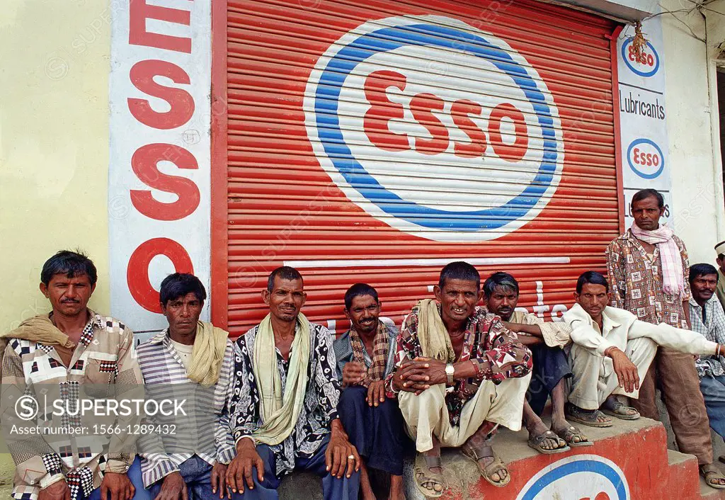 Day labourers waiting for a work under Esso trademark and logo. Udaipur Rajasthan, India.