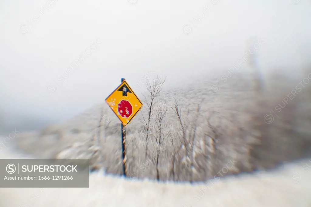 Distorted and blurred lensbaby photograph of a roadsign in snow warning of a coming stop sign ahead.