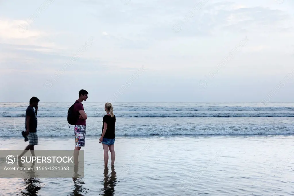 Palolem, India-September 1, 2012. A couple of tourists chatting on the shore as the tide rises and the sky begins to sunset.