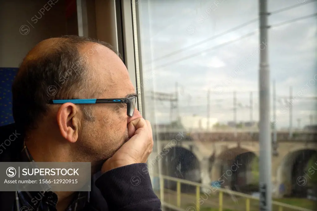 Middle-aged man, with glasses, looking through the window of a train. Italy, Europe