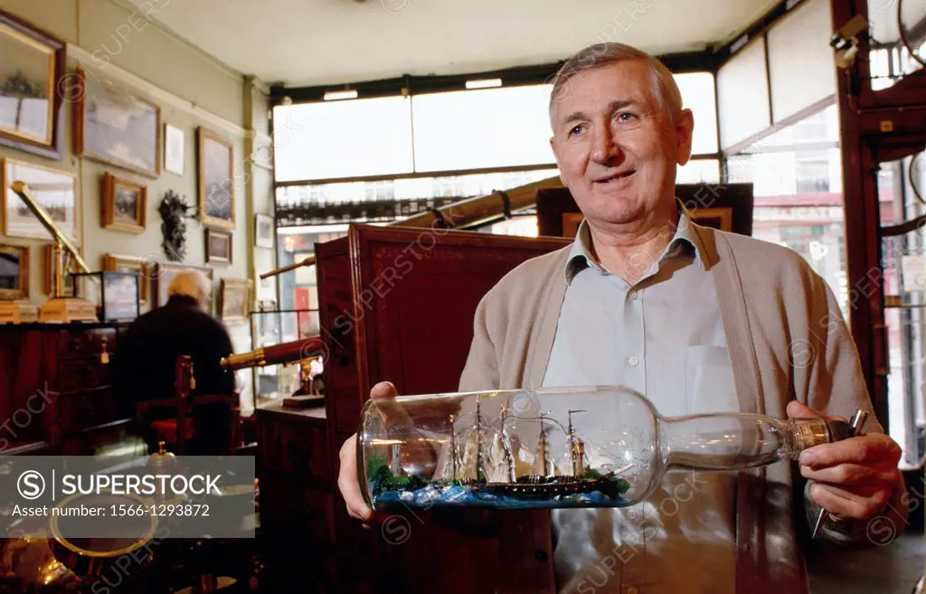 UNITED KINGDOM LONDON GREENWICH ANTIQUE MARITIME DEALER IN HIS SHOP HOLDING A SHIP SCALE MODEL BUILT IN A GLASS BOTTLE MR / ROYAUME-UNI LONDRES GREENW...