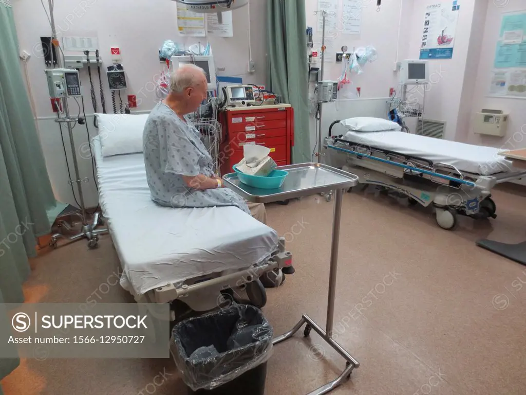 A senior man sitting on an examination bed in emergency at a hospital waiting for a doctor
