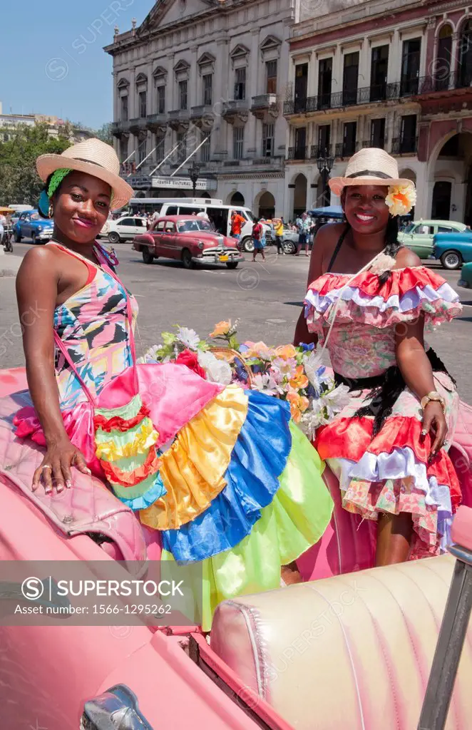 Havana Cuba local women with flowers at Capital in pink Classic Ford auto and hats smiling for tourists.