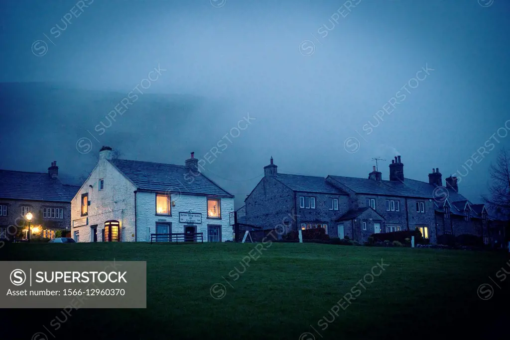 View of a village cottages with lights on in the windows and smoke in the chimneys on a cold winter day at dusk. Buckden, Yorkshire Dales, Skipton, En...