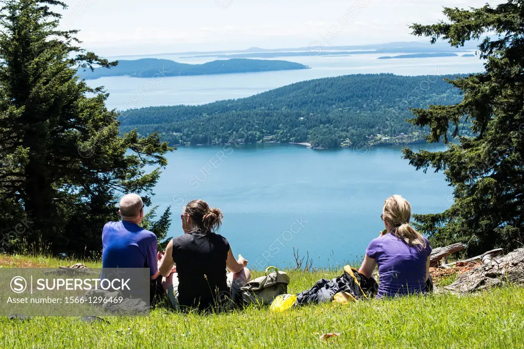 Three people enjoy the view from Mount Warburton Pike, a mountain on Saturna Island in the Gulf Islands of British Columbia, Canada. It is the highest...