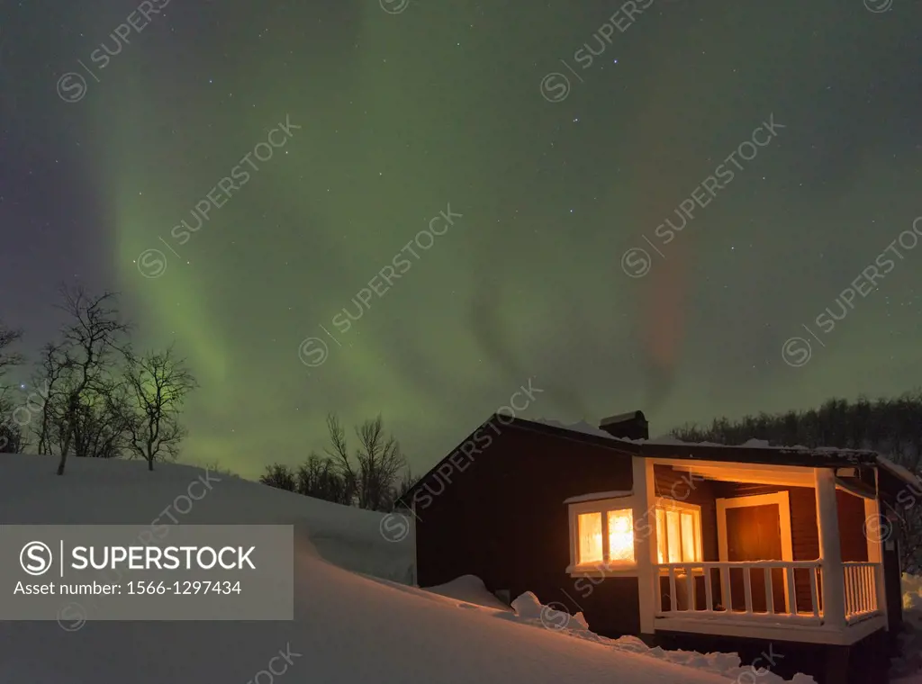 Northernlight, Aurora borealis, over a cottage with light coming through the window in winter season in march, in Riksgränsen, Swedish lapland, Sweden...