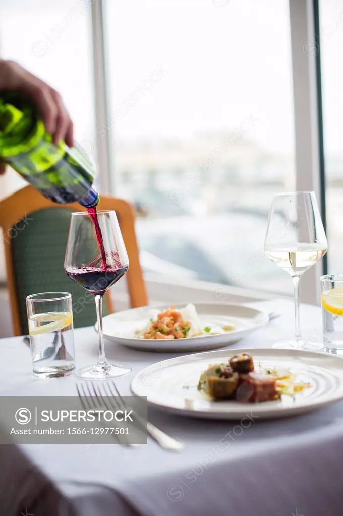 Pouring a glass of red wine to accompany a meal lunch dinner for two in a hotel restaurant.