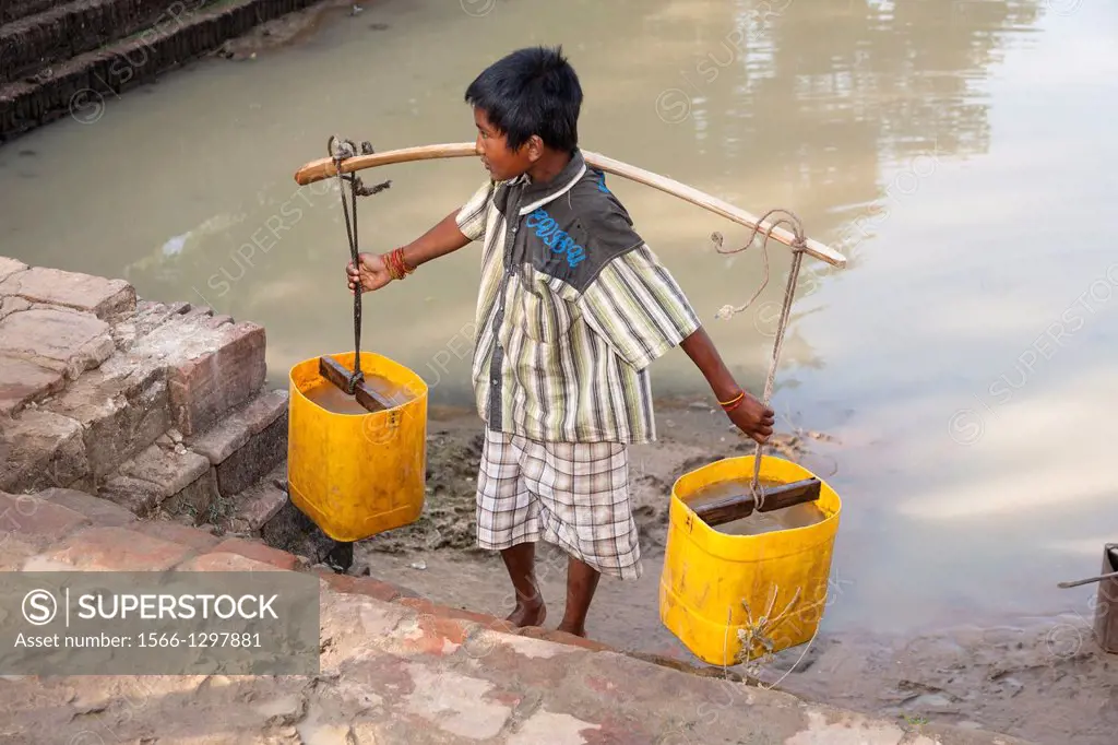 Young boy carrying a pannier filled with water, Minnanthu, Bagan, Myanmar, (Burma).