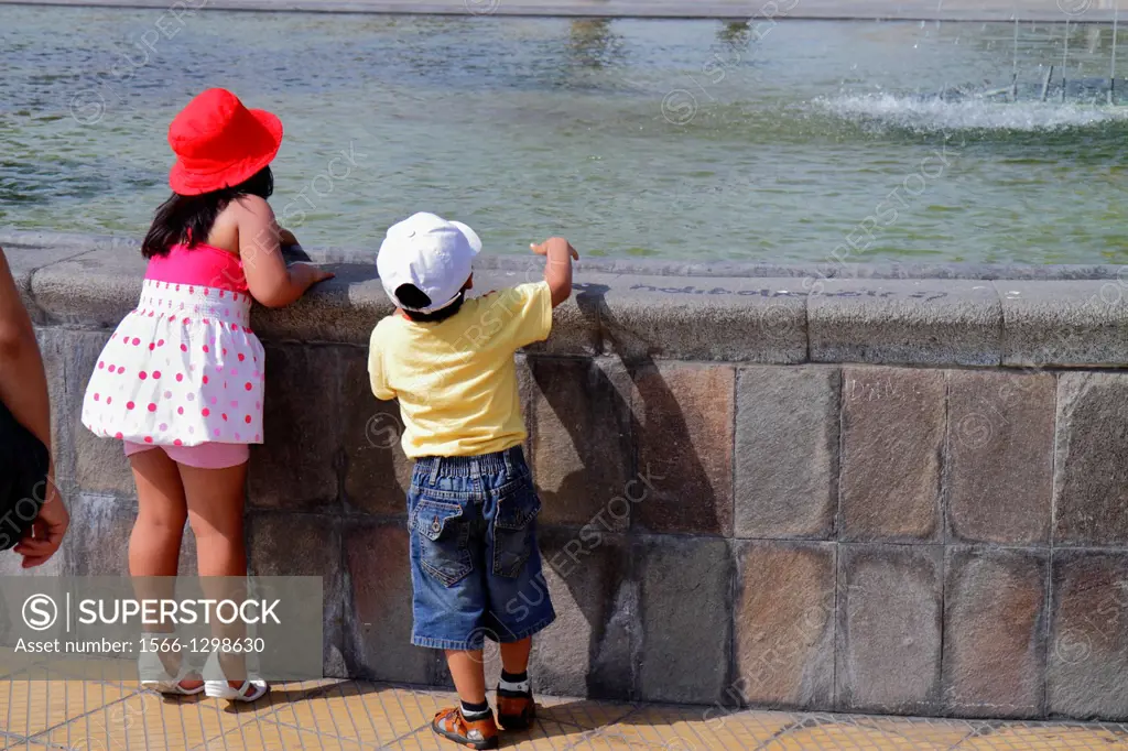 Peru, Lima, Miraflores, Malecon de la Reserva, Parque Salazar, urban park, fountain, water, stone ledge, Hispanic, boy, girl, child, standing on tipto...