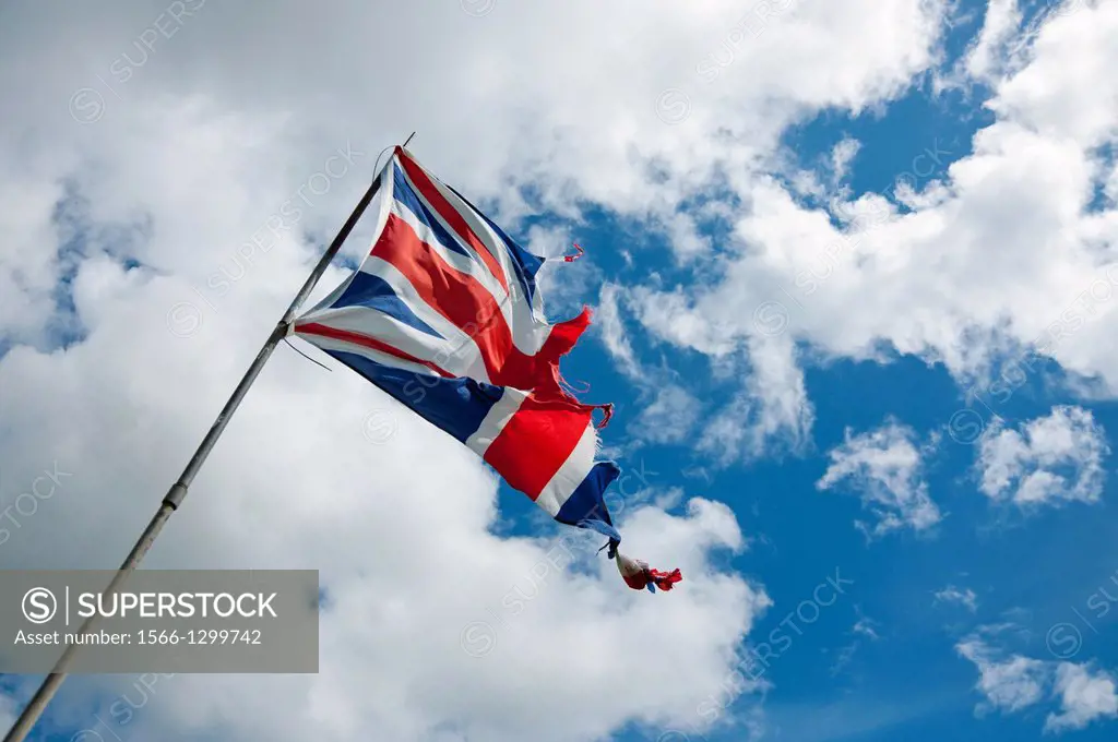 A tattered British Union flag is seen flying against a blue sky.  