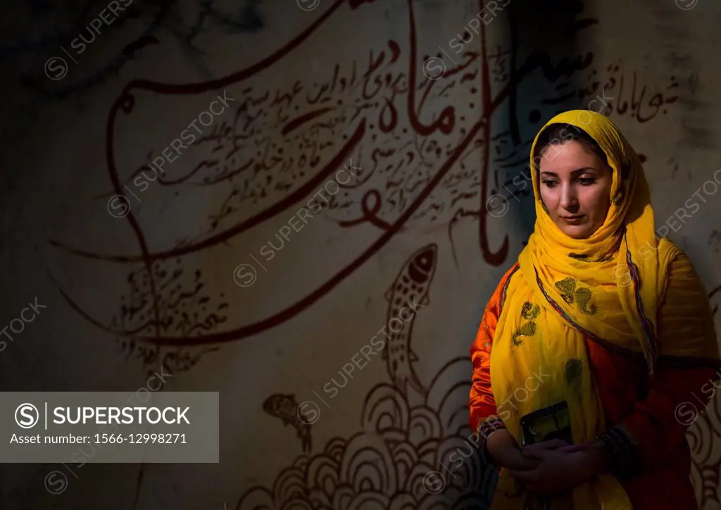 Iran, Qeshm Island, Salakh, portrait of beautiful young veiled woman in front of iranian calligraphy.