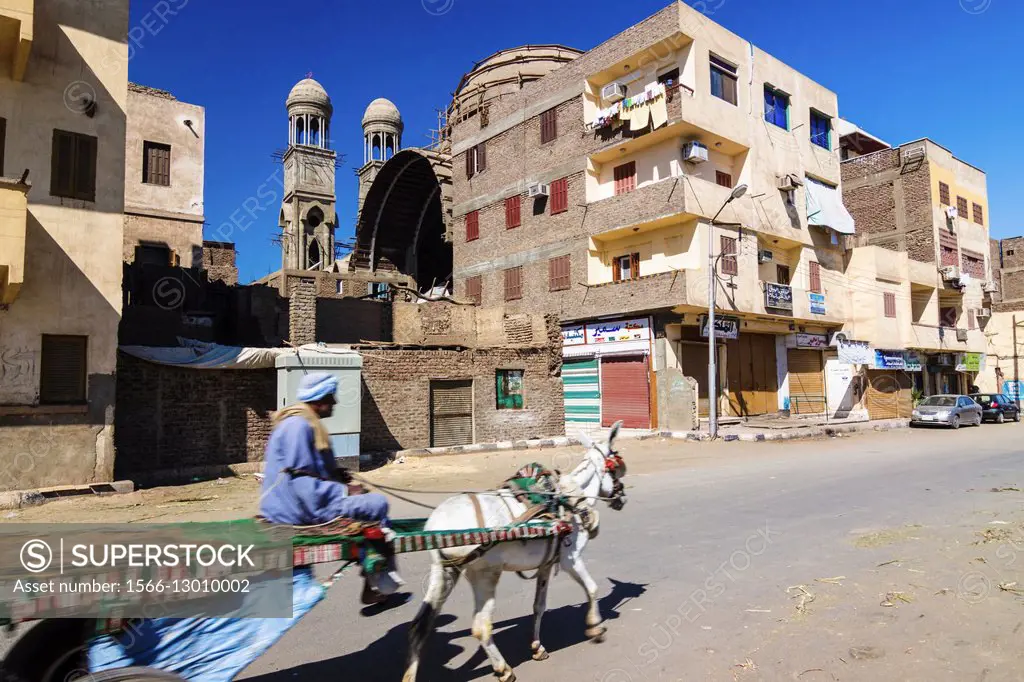Man in a donkey cart passing by the still in construction new Coptic cathedral of Luxor, Egypt.
