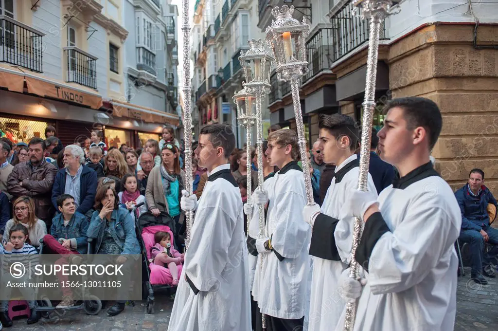 A group of teengage altar boys in robes bear ornate candle holders during a Semana Santa (Holy Week) procession in the historic center of Cádiz.