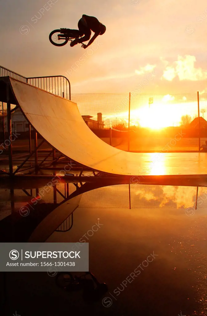 BMXer riding a halfpipe in Swansea, South Wales during a sunset, rider silhouetted with his reflection in a puddle.