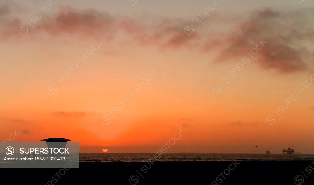 Sunset silhouette of beach hut in california with oil rig in background.