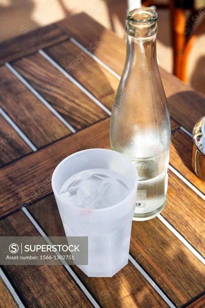 Bottle of Water and a Glass of Iced Water Sitting on a Beach Table.
