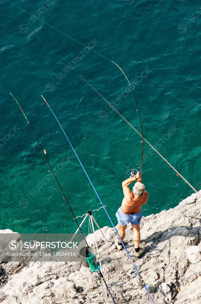 Fisherman on the cliffs draws angling with his fishing pole, around him a number of other fishing rods