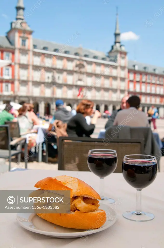 Fried squids sandwich with two glasses of red wine in a terrace. Main Square, Madrid, Spain.
