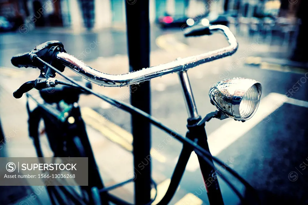 Close-up of the handlebar and lamp of a Dutch bicycle parked on a lamppost, on a rainy day. London, England, UK, Europe.