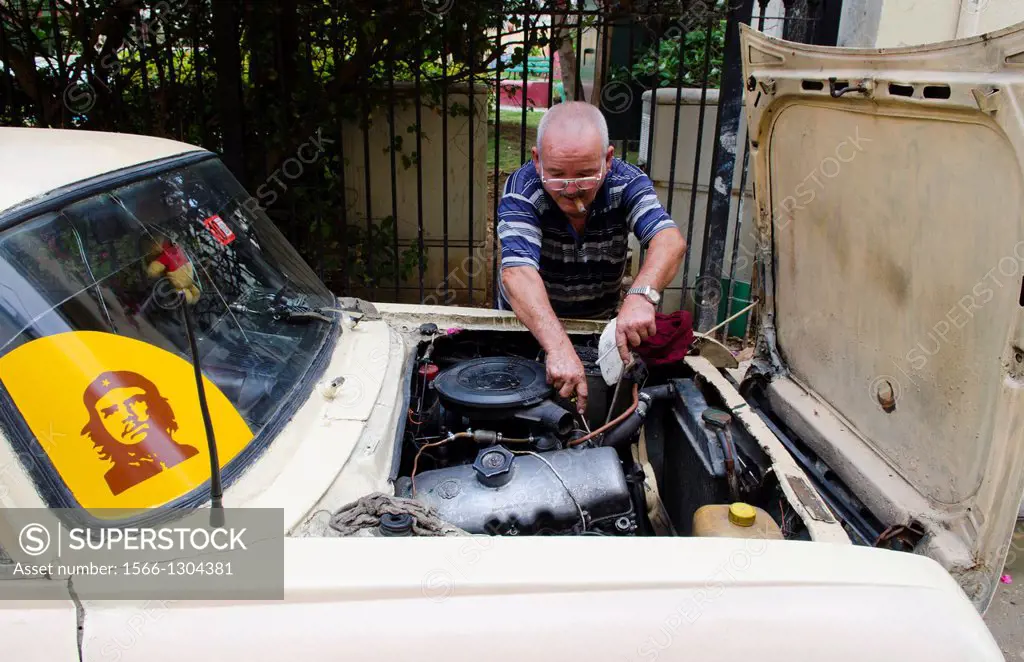 Havana Cuba typical scene in Cuba of man repairing old car on street with Che sticker on windshield.