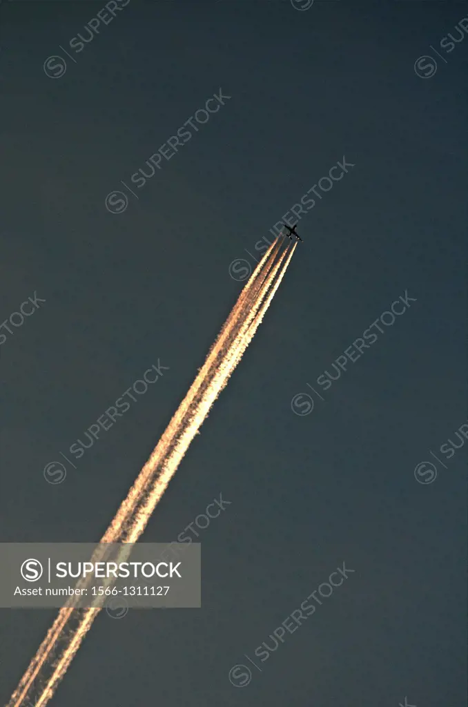 Passenger jet liner flying at high altitude leaving illuminated vapour trails against a dark sky