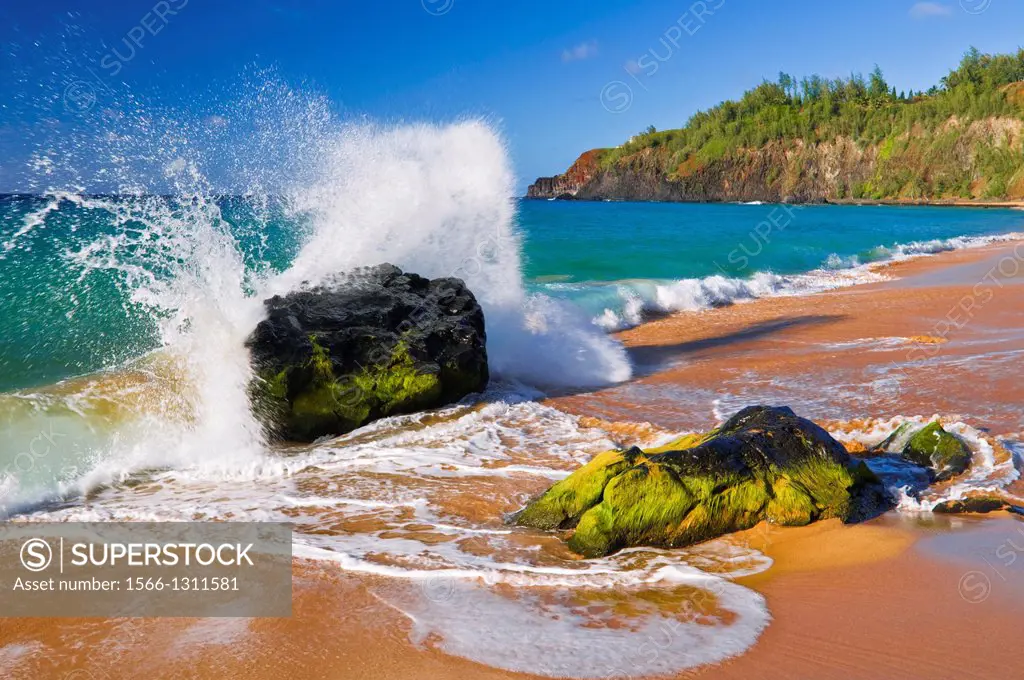Surf crashing on rocks at Secret Beach (Kauapea Beach), Kilauea Lighthouse visible, Kauai, Hawaii USA.